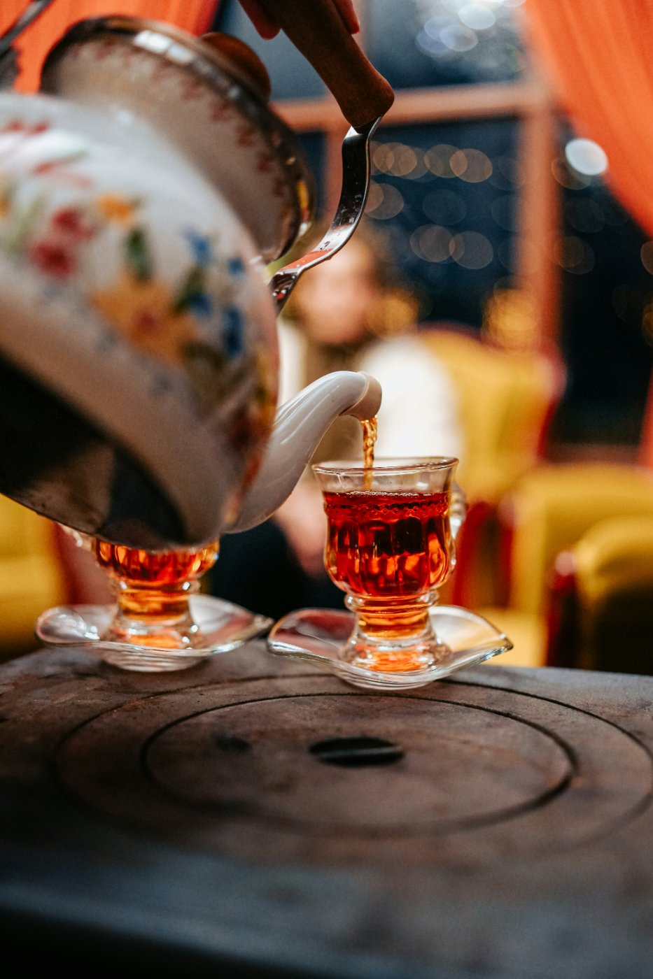 A pot of tea poured carefully into a small glass cup, evoking the warmth of hospitality and gathering.